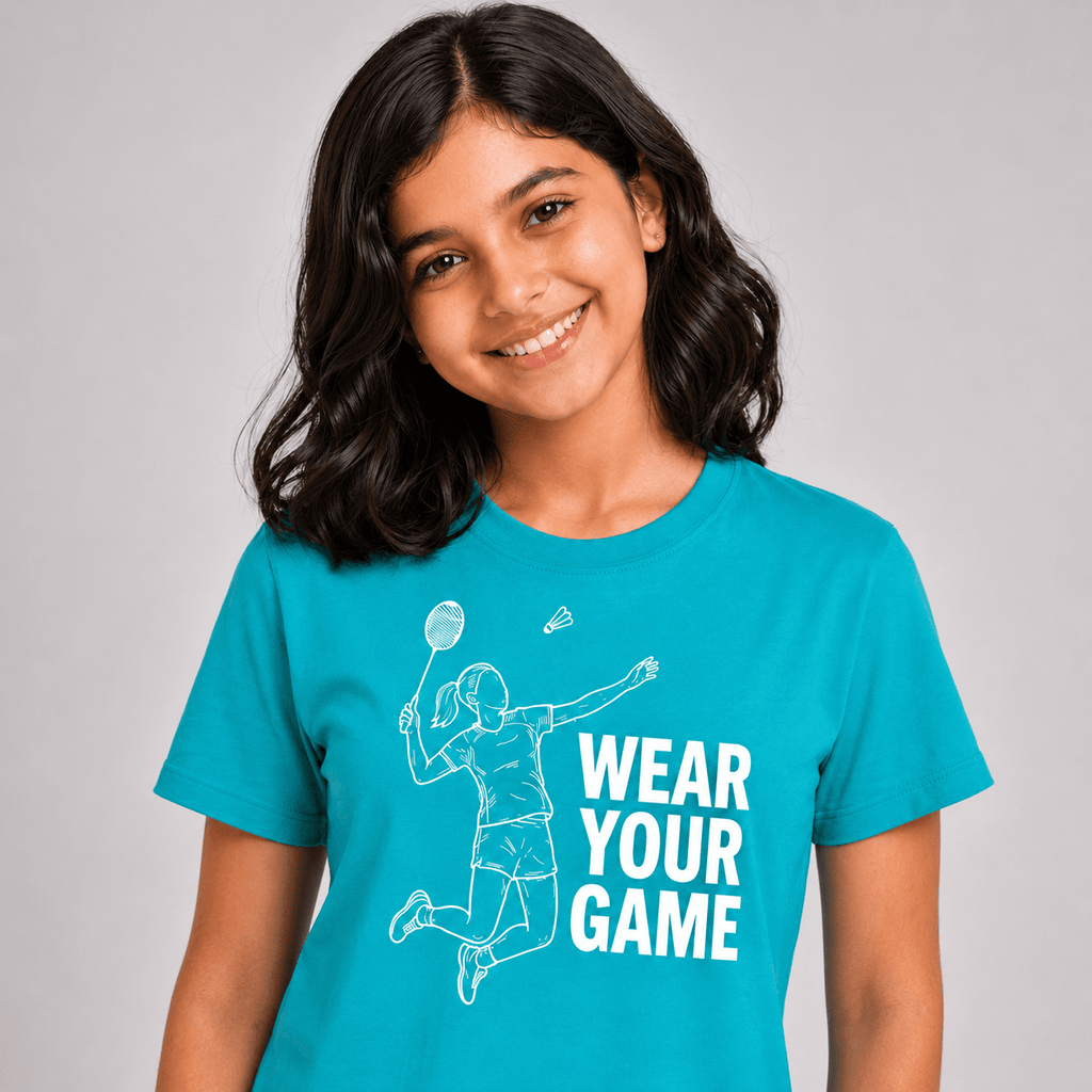 A smiling young woman with dark hair wearing a bright turquoise blue t-shirt with a white graphic of a badminton player and the text 'WEAR YOUR GAME'.