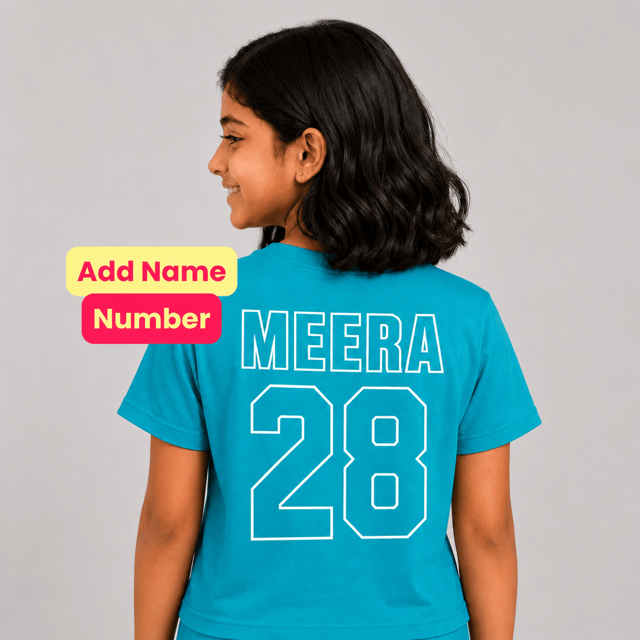 A child model shown from the back wearing a bright turquoise blue custom sports jersey with 'MEERA 28' printed in white outline text. The image includes a yellow and pink graphic overlay on the left reading 'Add Name Number'.
