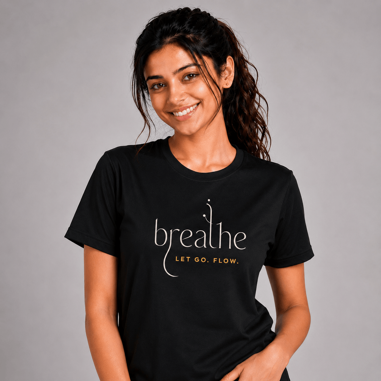 Woman wearing a black yoga t-shirt with 'breathe LET GO. FLOW.' text on a gray background