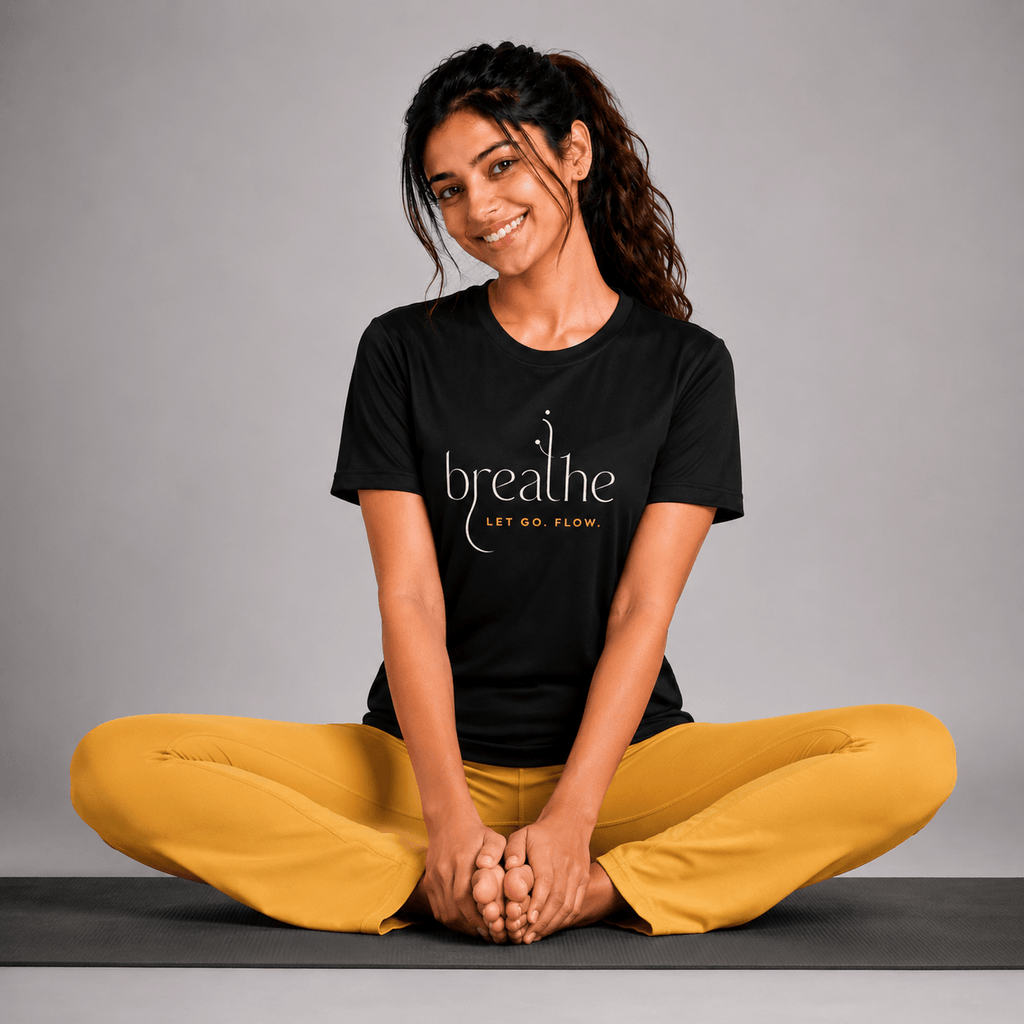 Woman sitting on a yoga mat wearing a black t-shirt with 'breathe' text and yellow pants against a gray background.