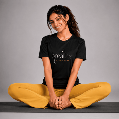 Woman sitting on a yoga mat wearing a black t-shirt with 'breathe' text and yellow pants against a gray background.
