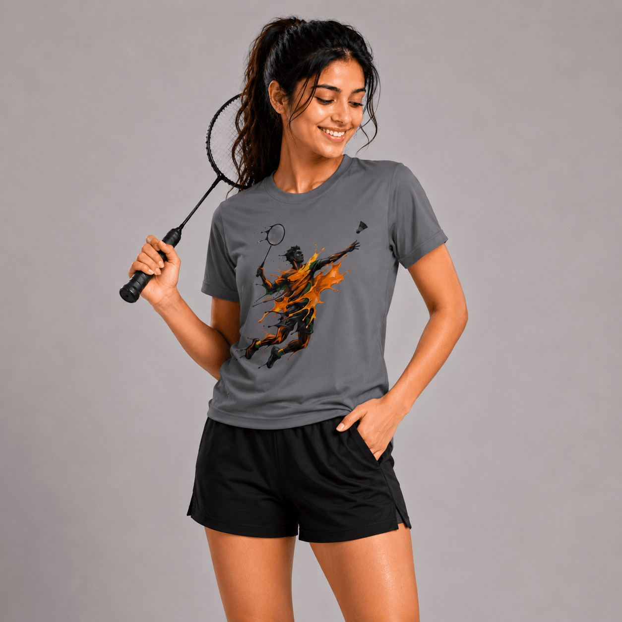Woman wearing a gray t-shirt with a graphic design, holding a badminton racket on a gray background