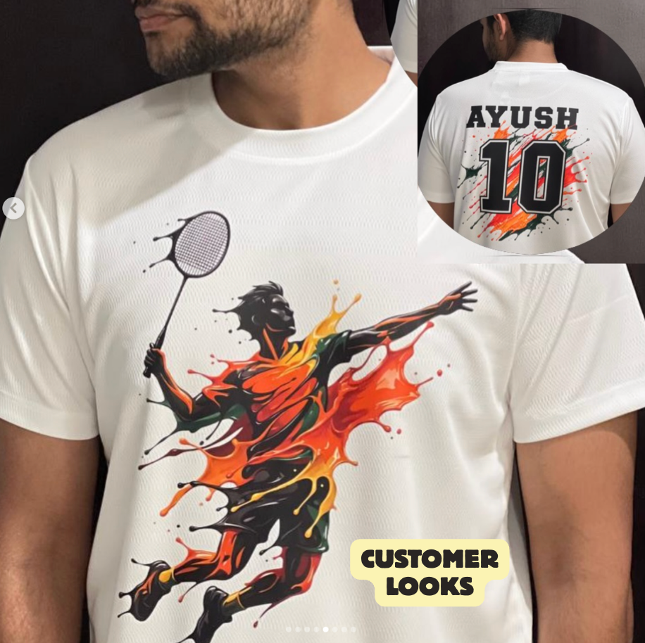 A man wearing a white short-sleeve graphic T-shirt with a large black, orange, and red badminton player print on the front. A circular inset shows the back of the shirt with the name AYUSH and number 10 printed in black with orange and red accents.