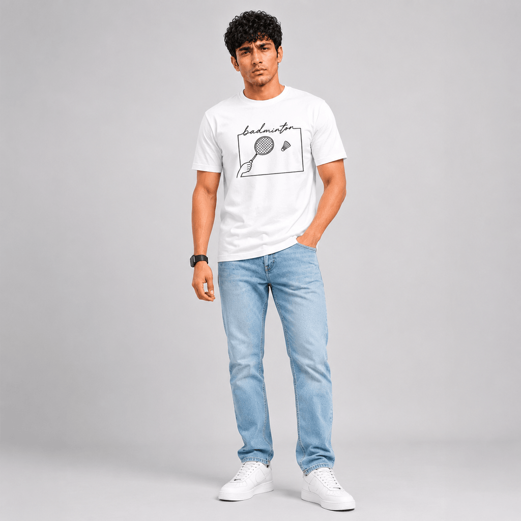 A man modeling a white short-sleeve t-shirt with a black hand-drawn badminton graphic on the chest, paired with light blue jeans and white sneakers, against a solid gray studio background.