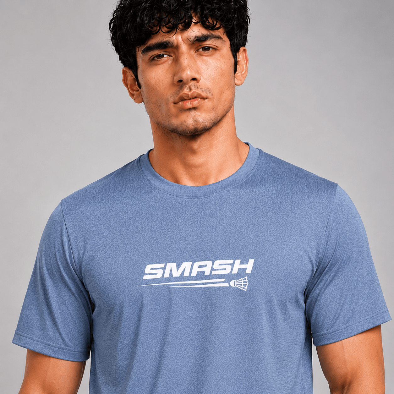 A man wearing a heathered blue crewneck t-shirt with a white 'SMASH' logo printed across the chest, set against a plain gray studio background.