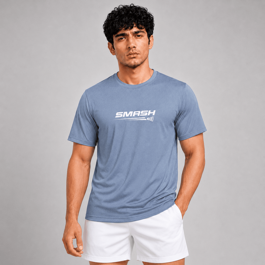 A man wearing a heathered blue crewneck t-shirt with a white 'SMASH' logo on the chest, paired with white athletic shorts, set against a solid gray studio background.