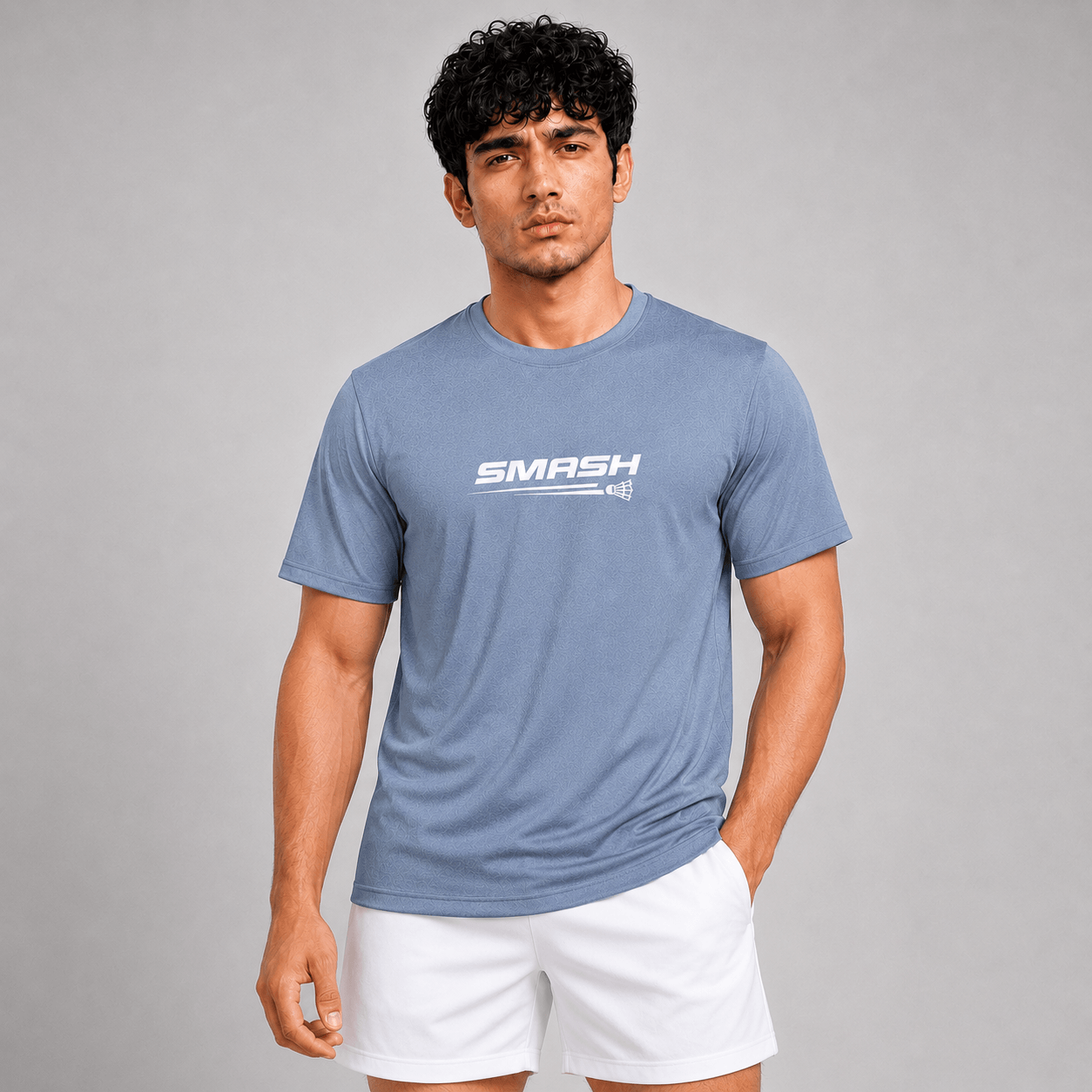 A man wearing a heathered blue crewneck t-shirt with a white 'SMASH' logo on the chest, paired with white athletic shorts, set against a solid gray studio background.