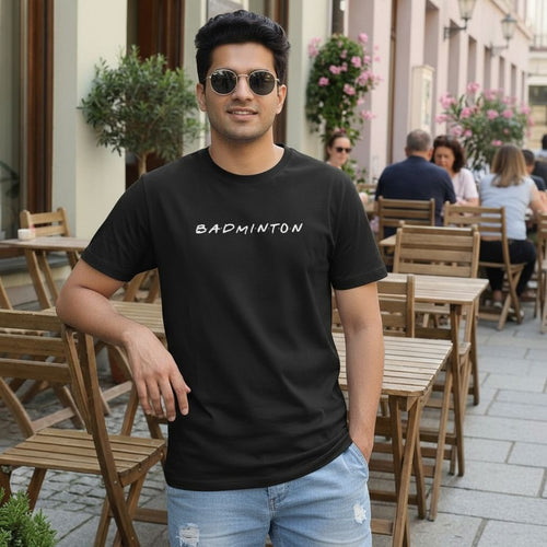 Man wearing a black t-shirt with 'BADMINTON' text in an outdoor setting.