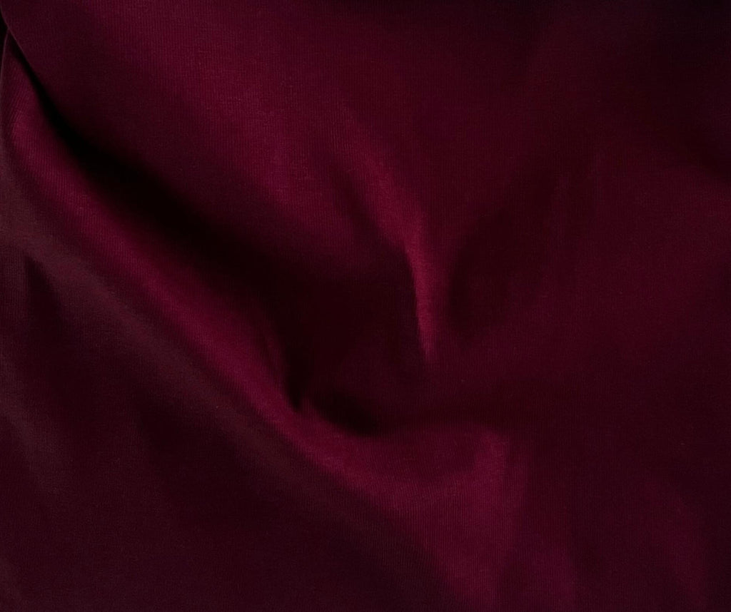 A close-up of draped deep burgundy fabric with soft folds and a smooth texture.